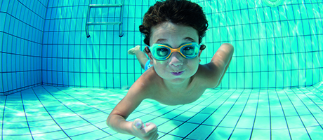 Pojke med somglasögon som simmar under vatten i en simbassäng